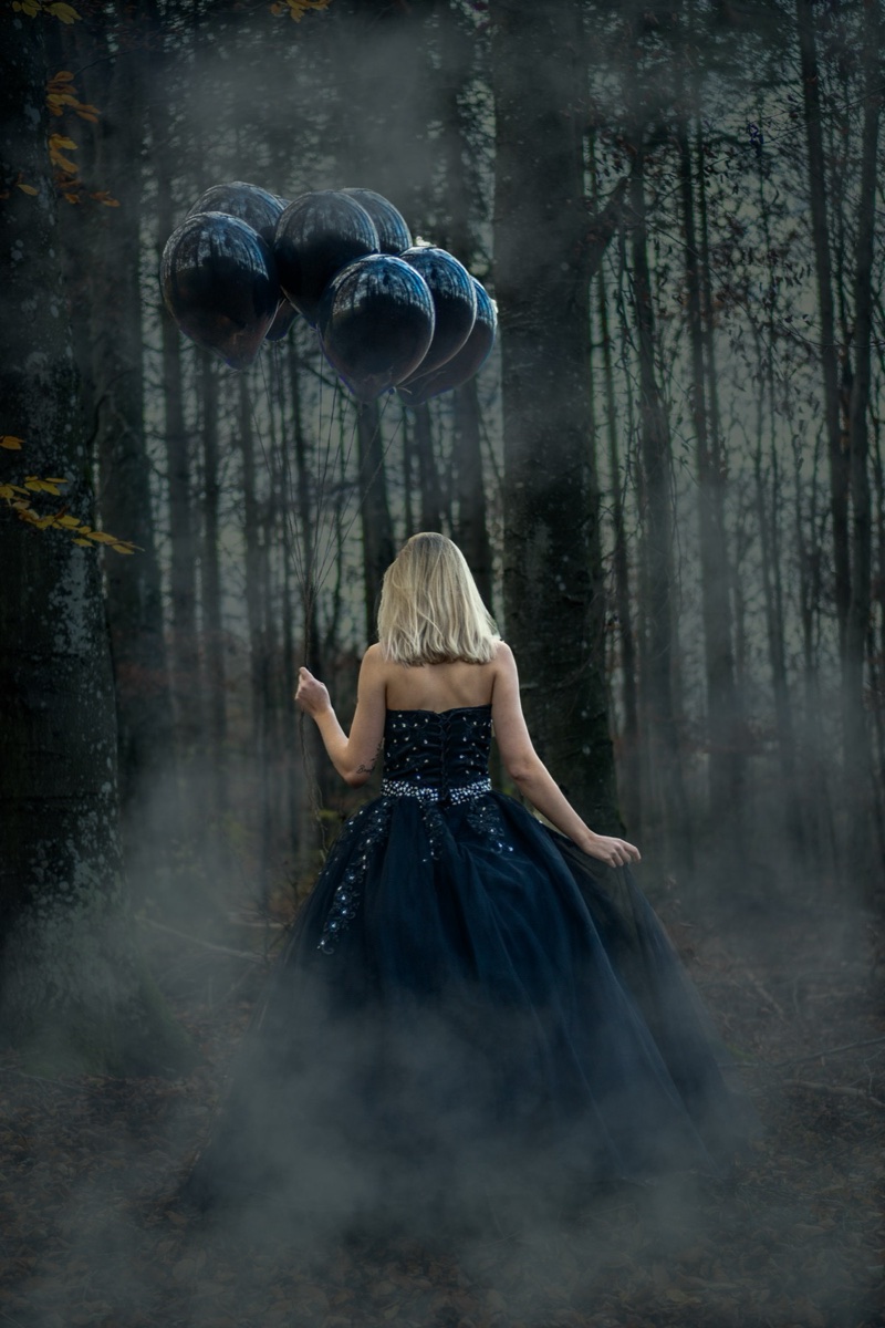 Conceptual portrait with black balloons in a forest